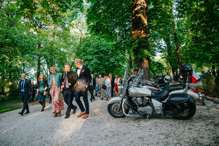 goście idą przez ogród na wesele mijając motocykle 