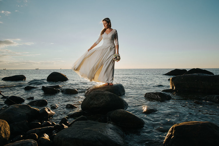 Portret panny młodej nad morzem podczas sesji zdjęciowej o wschodzie słońca na kamienistej plaży w Gdyni Orłowo