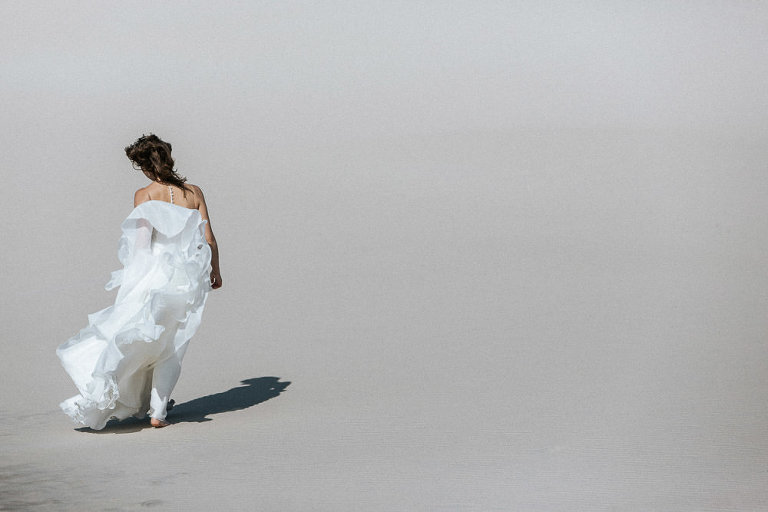 Pani młoda idzie dziką plażą podczas sesji ślubnej nad morzem 